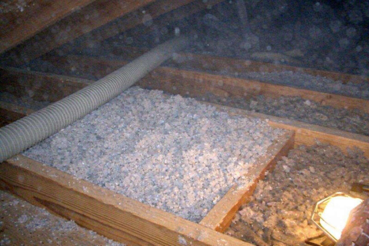 A blowing hose laying fresh loose-fill insulation between bare attic joists