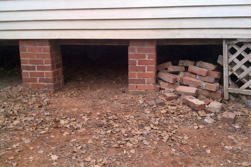 A dark gap running between the brick piers under the floor line of an older house