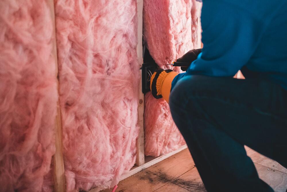 A worker in gloves fitting mineral wool insulation into a wall cavity, seen from the side