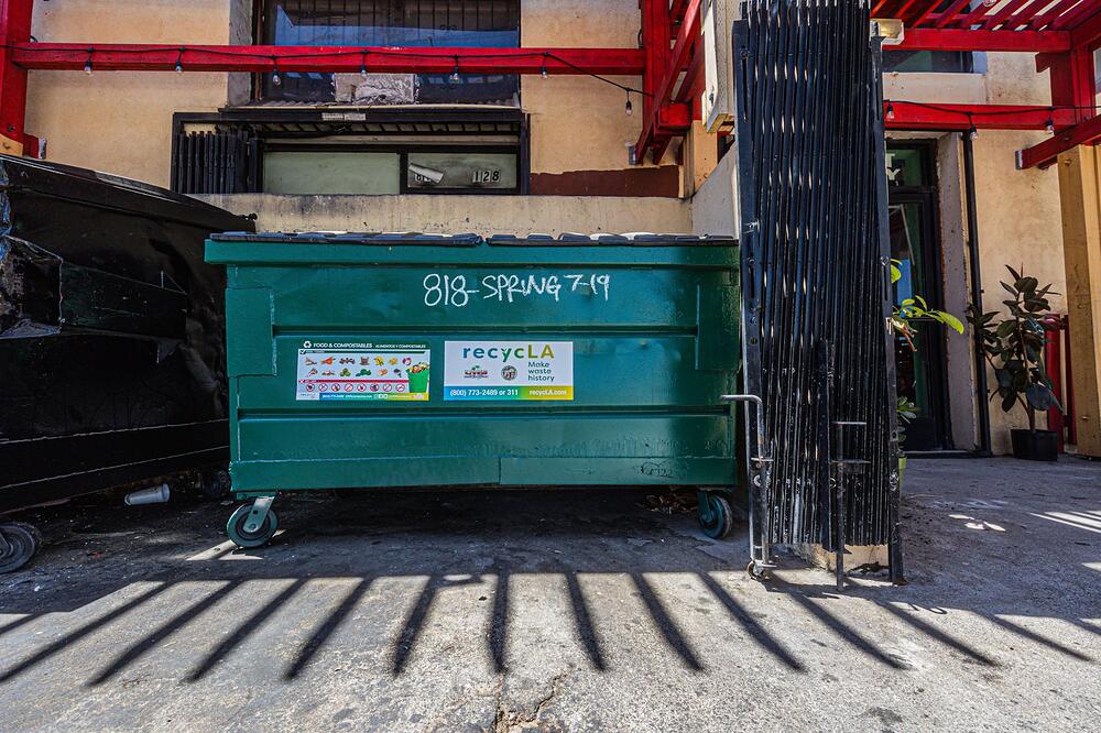 A green dumpster standing on the pavement against the back wall of a commercial building