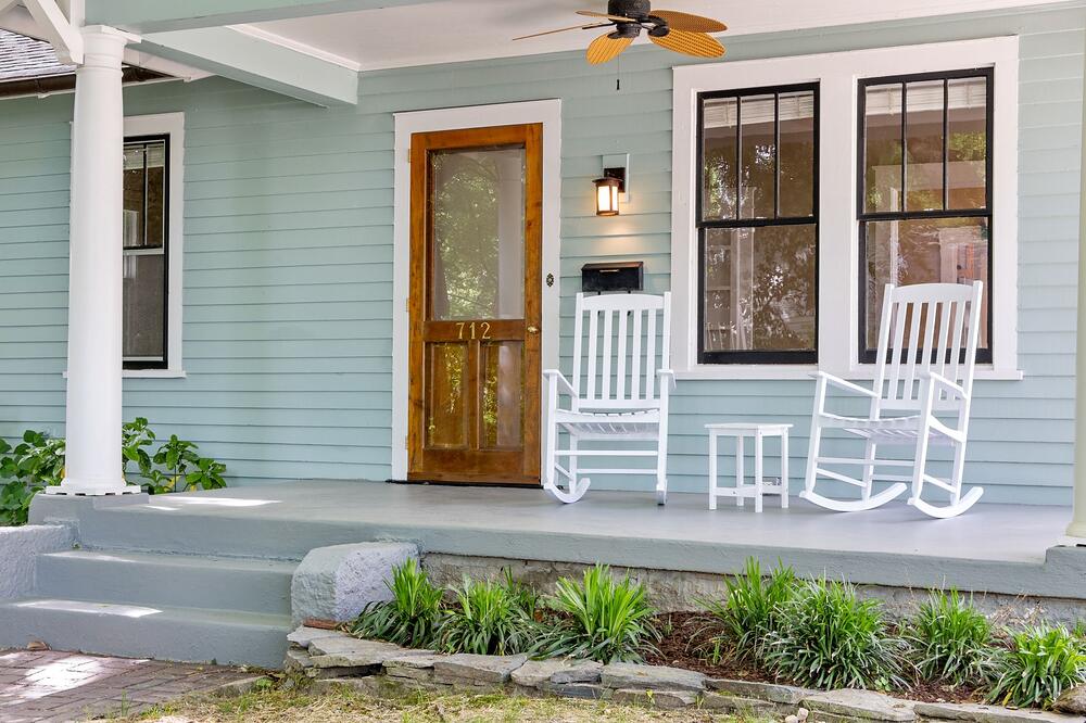 A front porch with white rocking chairs beside a wooden front door