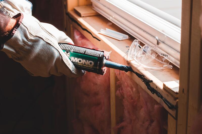 A gloved hand running a bead of sealant along a seam during exterior work