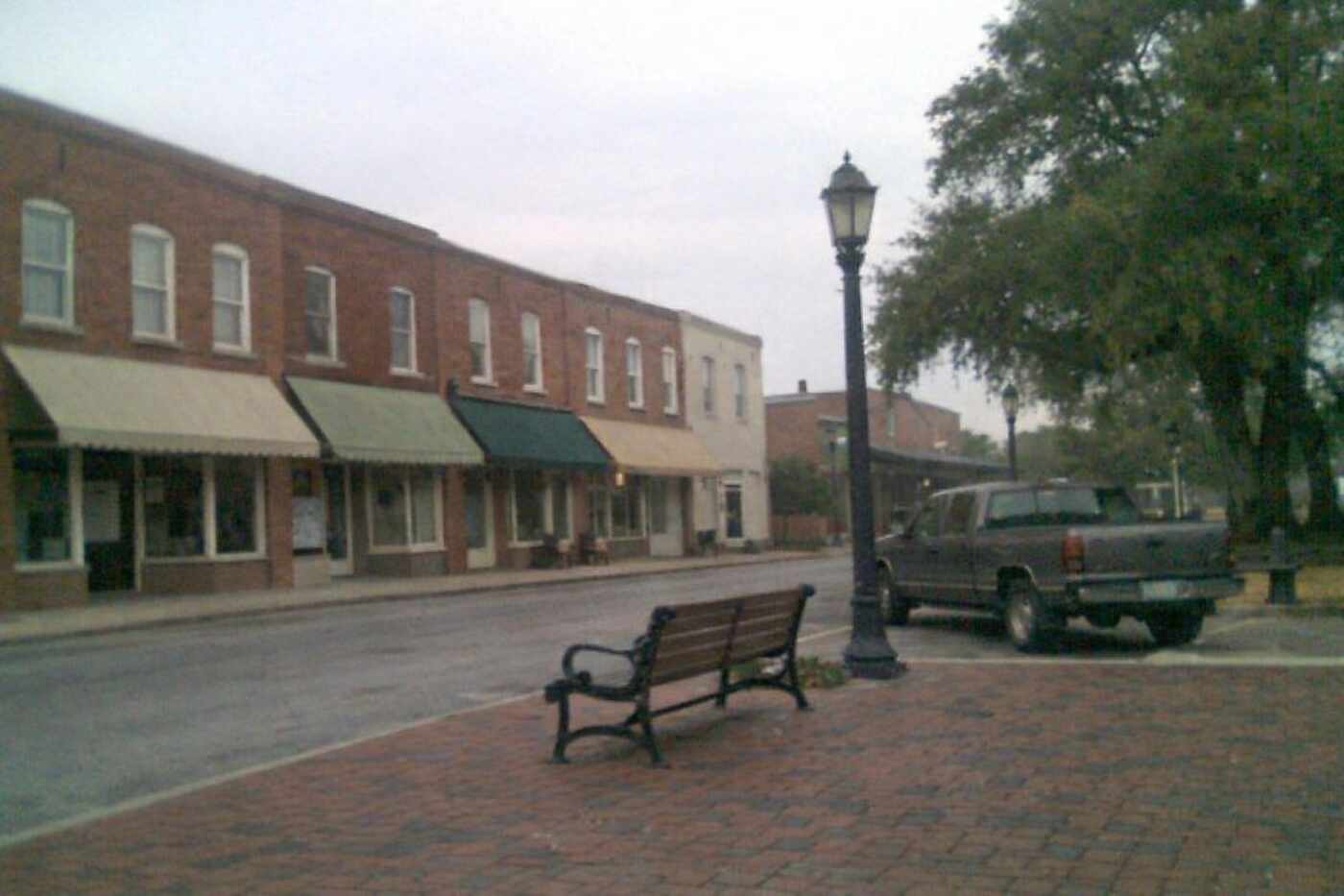 A row of two-story brick storefronts with awnings facing a small town square