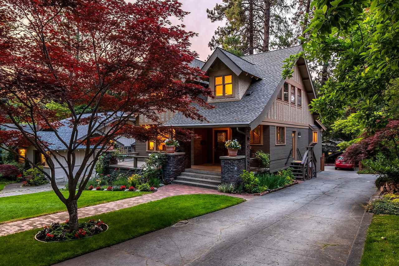 A substantial house set back on a wooded lot with a red maple beside it at twilight