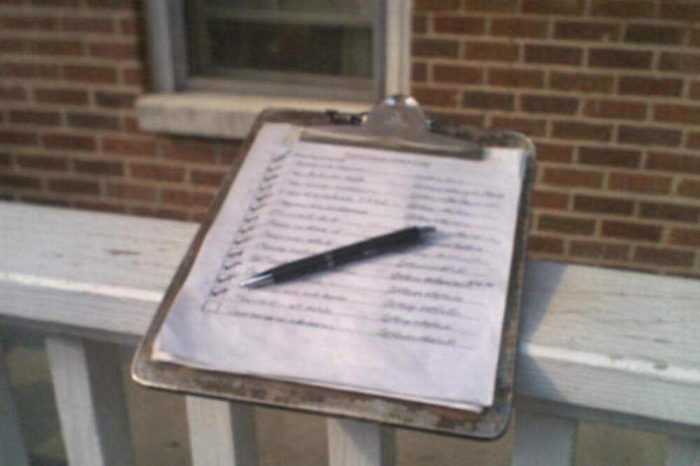 A completed inspection checklist on a metal clipboard resting on a porch rail with a pen across it