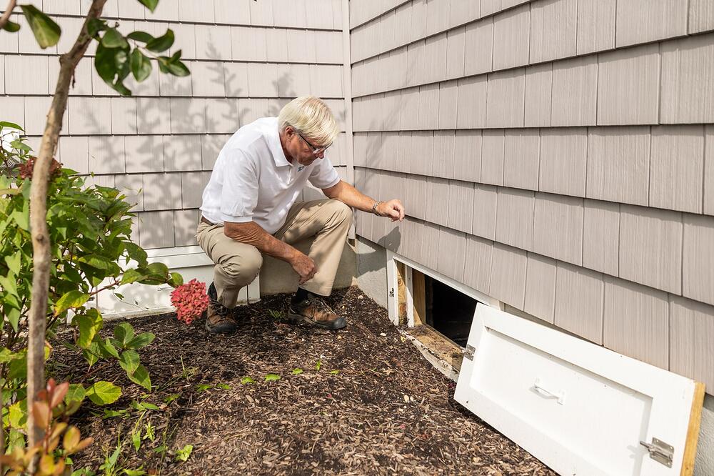 A person crouched at the open access door of a crawl space during a home inspection