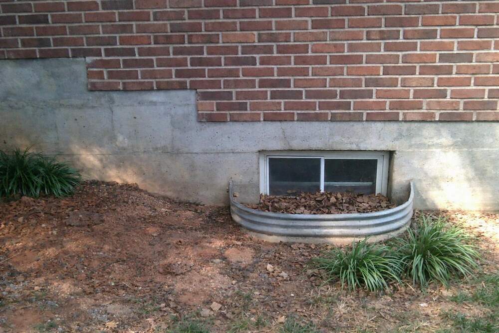 A concrete foundation wall stepping down to a basement window in a metal window well