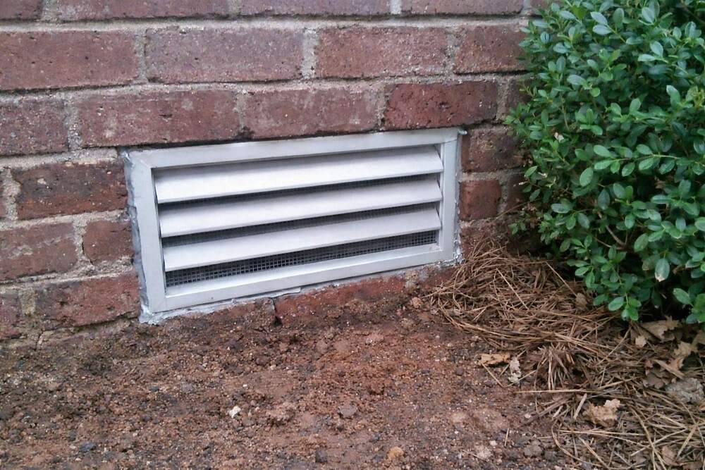 A louvered crawl space vent in a brick foundation wall with new metal screening fitted behind the slats