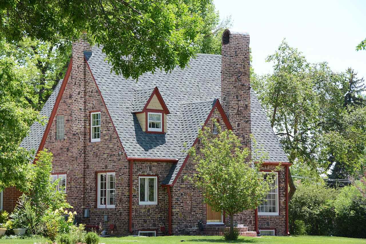 The steep brick and stucco gable of a small cottage under heavy tree cover