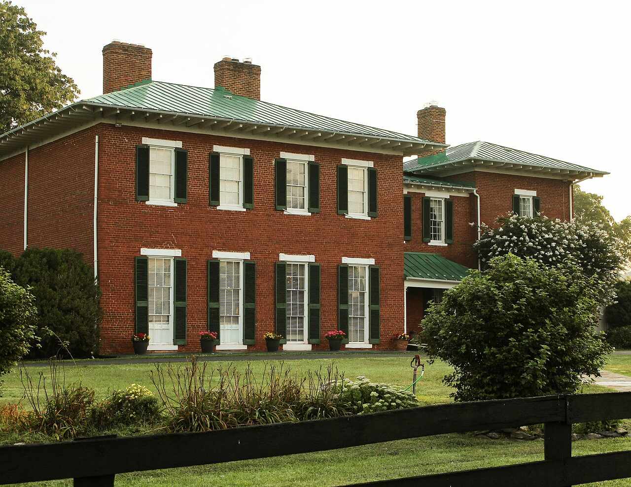 A two-story brick house with shutters, a columned entry and a clipped lawn