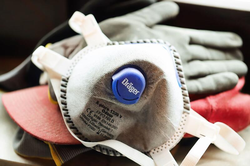 A half-face respirator and a pair of work gloves resting on a bench